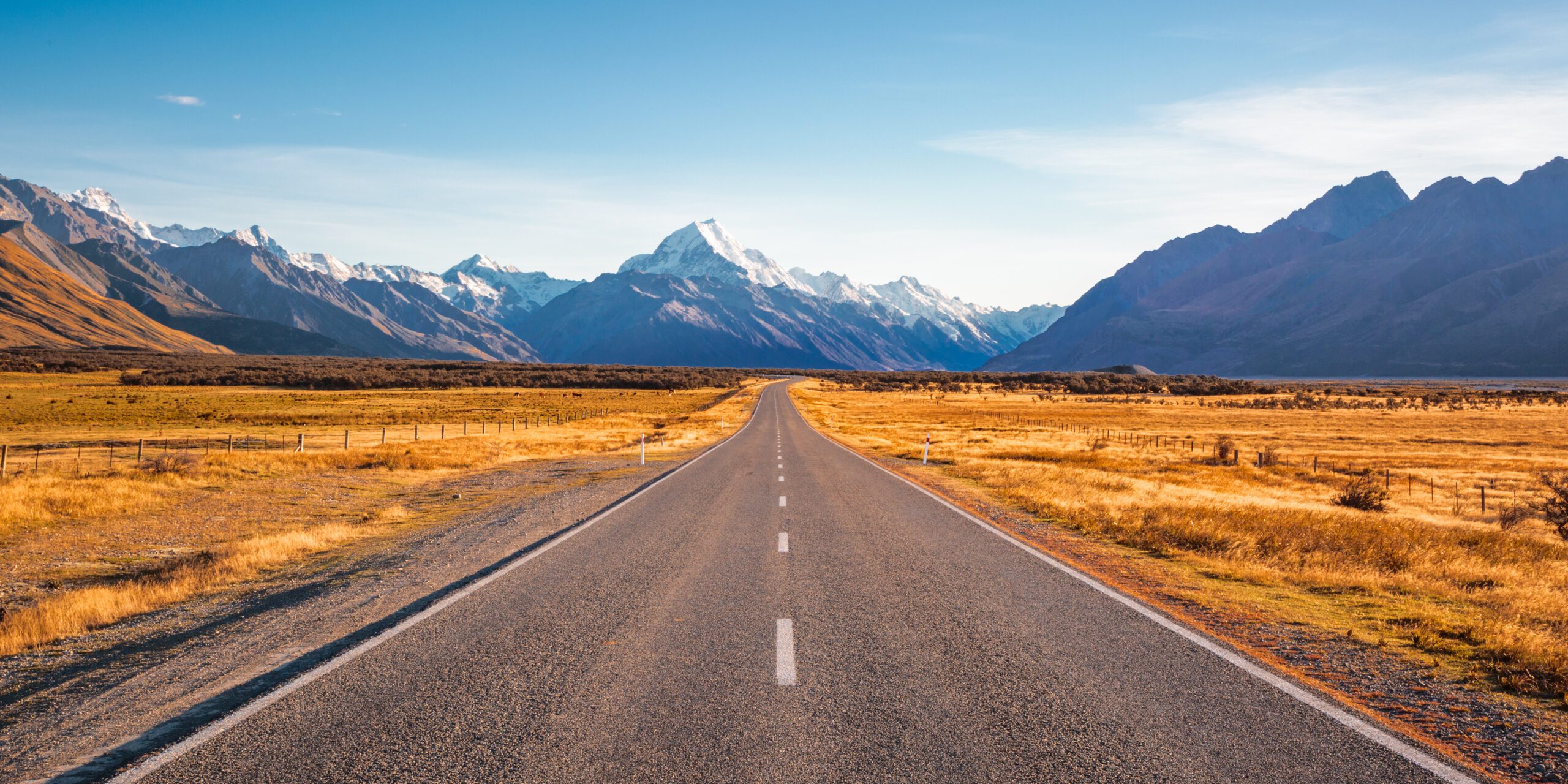 A,long,straight,road,leading,towards,a,snow,capped,mountain